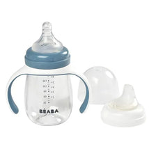 2-in-1 Beaba bottle to sippy learning cup with blue lid and handles, clear body with measurement markings, includes an extra spout.