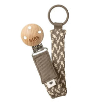 Bibs pacifier clip in dark oak and vanilla, featuring a wooden clip and woven strap with a heart design.