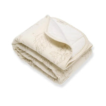 Reversible cream blanket with a subtle tree branch pattern, folded with soft texture and striped backing.