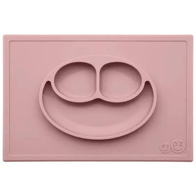 Silicone feeding mat in blush color featuring a smiling face design with two compartments for food.