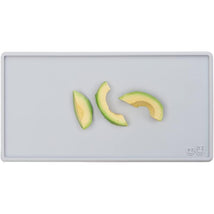 Tiny pewter-colored placemat with three avocado slices arranged on it.