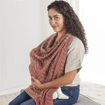 Breastfeeding mother wearing an Itzy Ritzy multi-use cover, featuring a brown fabric with white diagonal lines.
