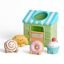 Colorful bakery toy set featuring a green Itzy Bakery shop and cute pastry figures, including a croissant, donut, and cupcake.