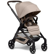 Lightweight Joolz Hub² compact stroller in sandy taupe with a large sun canopy and safety harness, featuring a storage basket below.