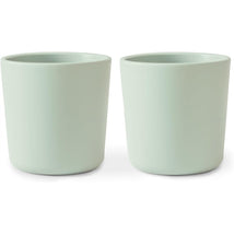 Two sage green silicone cups from the Mushie Silicone Dinnerware Cup Set, highlighting their modern, minimalist design.