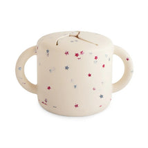 Mushie Snack Cup in cream with colorful star patterns, featuring two handles and a slot for easy snacking.