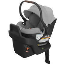Uppababy Aria Infant Car Seat in Light Grey, featuring adjustable handle, protective canopy, and safety labels on the base.