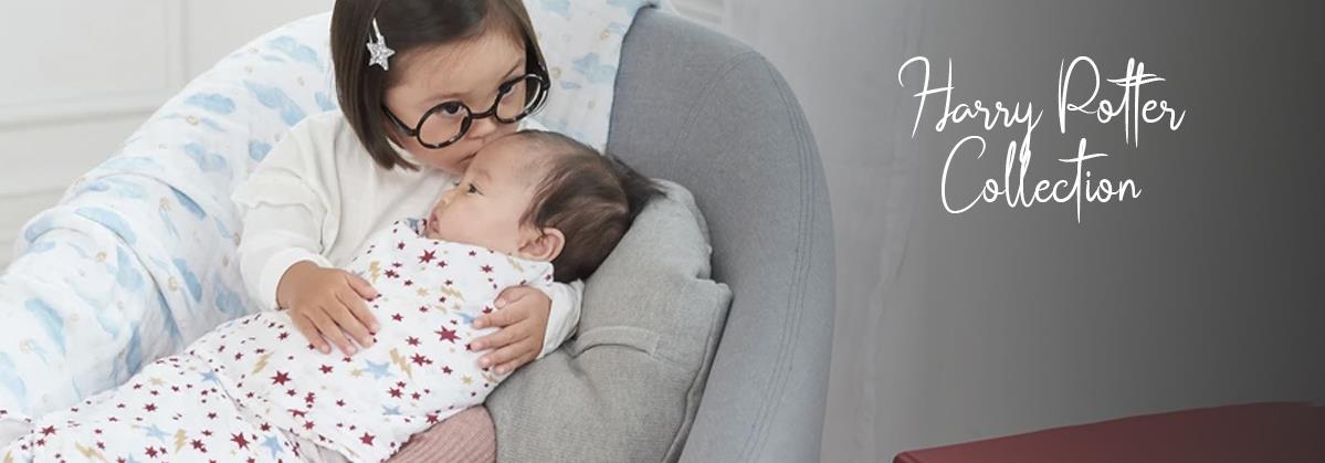 Toddler girl kissing baby in Harry Potter themed star print swaddle, cozy nursery setting