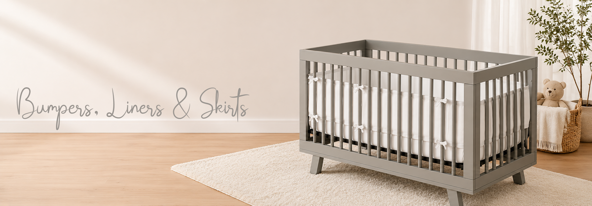 Gray baby crib with white bumper and bows, cozy nursery setting with rug and teddy bear