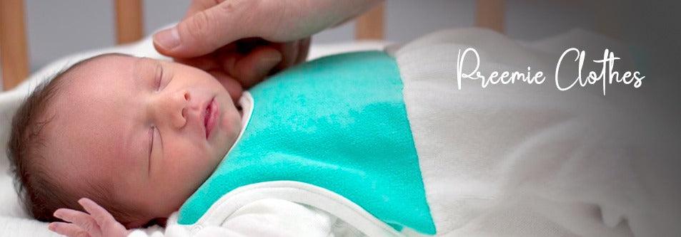 Newborn baby in preemie clothes, gently touched by hand, wearing turquoise and white outfit
