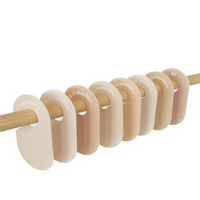 Baby and toddler hanger closet dividers in neutral colors, labeled with sizes from newborn to 2T, on a wooden rod.