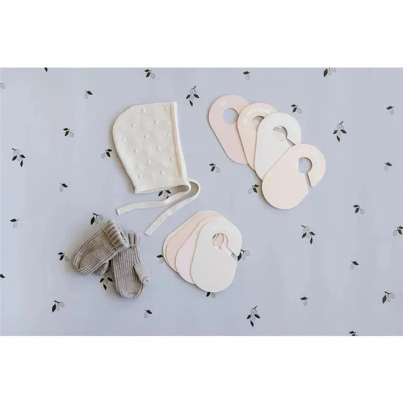 Baby cap, gray mittens, and eight neutral closet dividers on a floral background, showcasing a stylish organization solution.