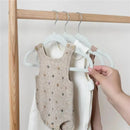 Blue velvet baby hangers are displaying a beige onesie with multicolored dots and two other garments on a wooden rack.
