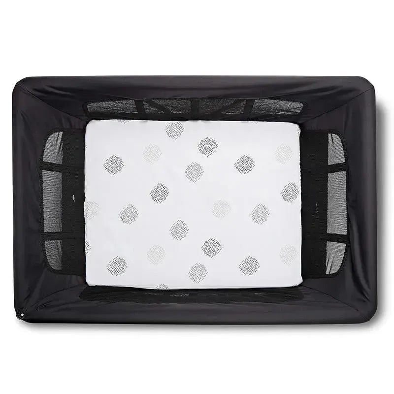 White bassinet sheet with a grey dotted pattern, fitted inside a black mesh-sided bassinet.
