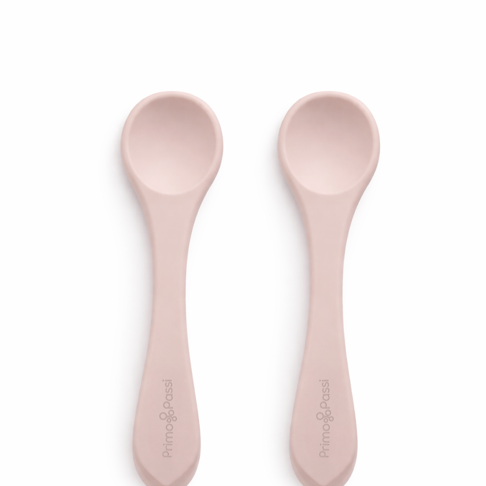 Two Primo Passi rose pink silicone baby feeding spoons on a white background.