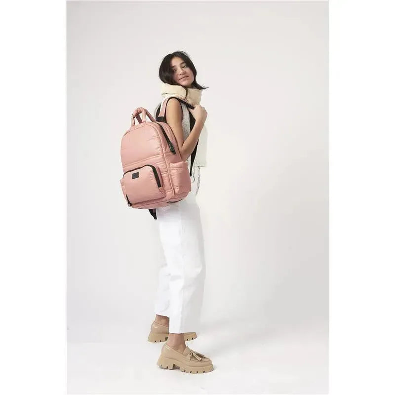 Diaper backpack in rose dawn color, being worn by a woman dressed in white pants and a light top.