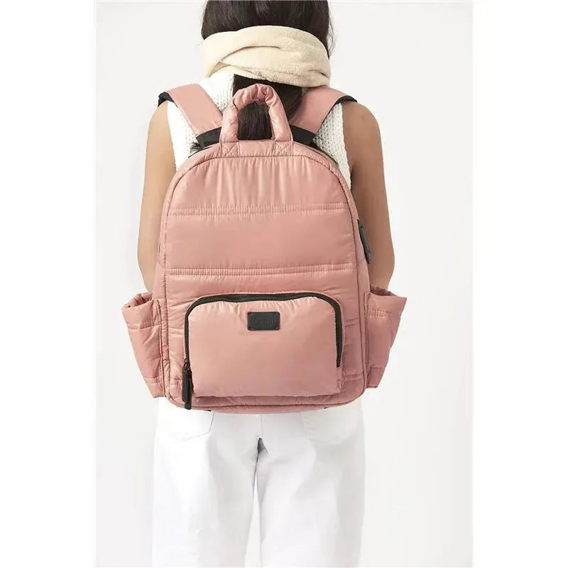 Diaper backpack in rose dawn color with padded design, adjustable straps, and exterior pockets, worn by a person.