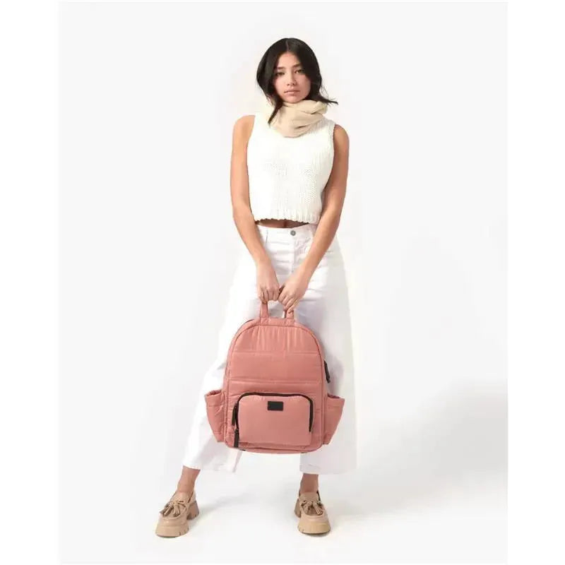 Diaper backpack in rose dawn color, held by a model wearing a white crop top and light pants.