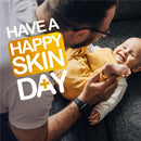Father playfully interacting with a smiling baby on a couch, with text promoting happy skin care.