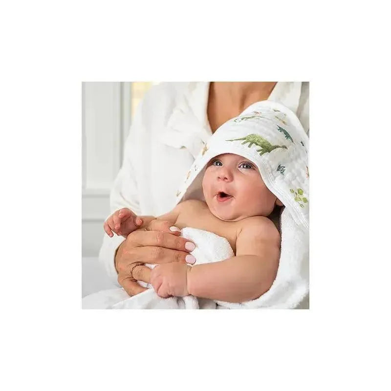 Baby wrapped in a hooded towel with a dinosaur design, smiling while held by an adult.