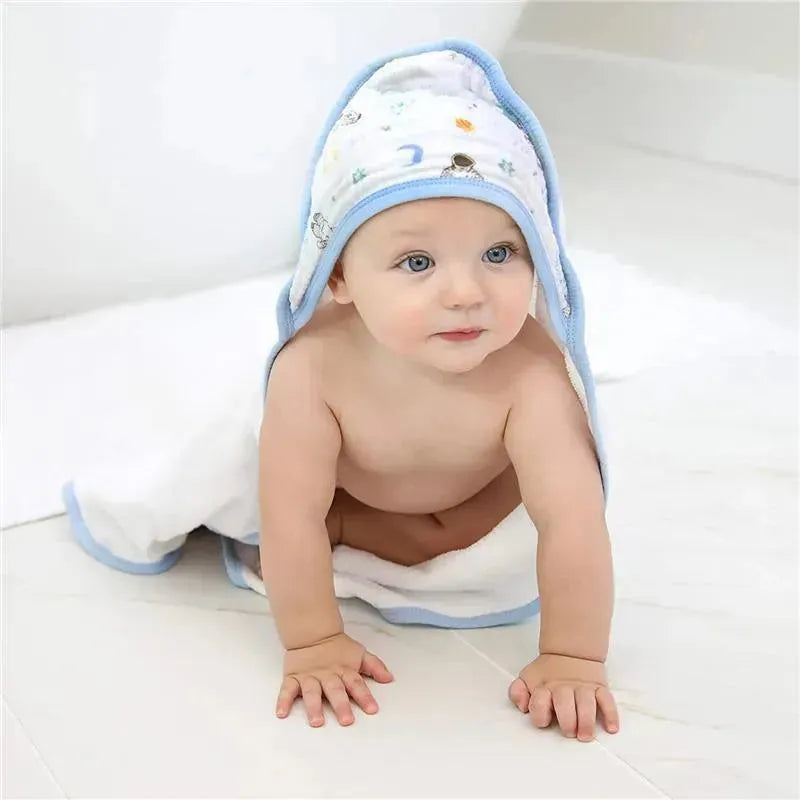 Hooded baby towel in blue and white, featuring space-themed designs, with a baby seated on a light floor.