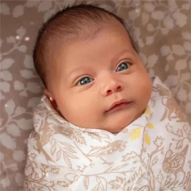 A baby wrapped in a soft, patterned Aden + Anais swaddle with woodland designs, featuring soft colors and floral elements.