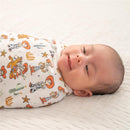 Baby swaddled in a colorful Aden + Anais wrap featuring Toy Story characters, lying on a textured surface.