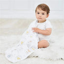 Toddler sitting on a soft surface, holding a white blanket featuring Winnie the Pooh characters, wearing a short-sleeve onesie.