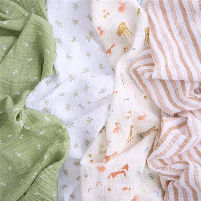 Four cotton muslin swaddles in sage green, white with woodland animals, and striped patterns, showcasing soft textures.