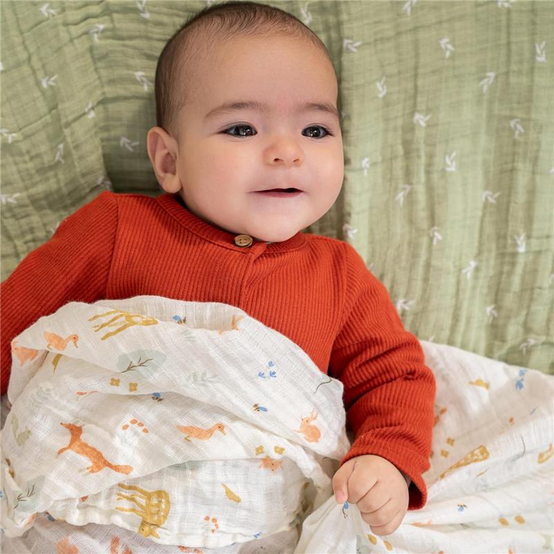 Baby wrapped in Aden + Anais 4Pk Essentials Cotton Muslin Swaddle, featuring animal prints, on a soft green background.