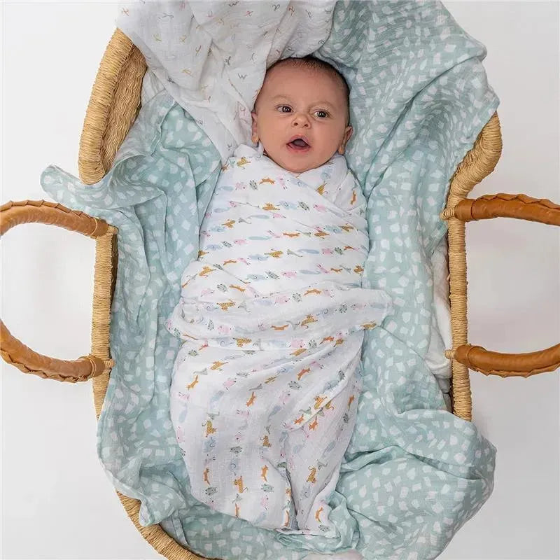 Aden + Anais muslin swaddles featuring playful animal prints, wrapped around a baby in a cozy bassinet.