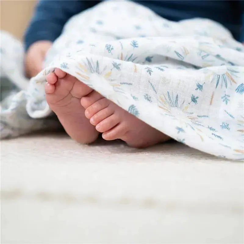 Infant feet peeking out from a soft, patterned muslin swaddle, showcasing gentle colors and delicate floral designs.