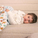 Toddler lying on a soft surface, wrapped in a Aden + Anais cotton muslin blanket featuring Toy Story characters.
