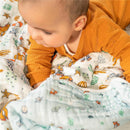 Baby playing on a multicolored Aden + Anais cotton muslin blanket featuring Toy Story characters Woody and friends.