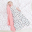Baby lying on a muslin blanket, wearing a Minnie Mouse sleeping sack and holding a pink Aden + Anais muslin blanket.