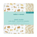 Muslin blanket featuring a Tanzania-Great Migration design with various animals and foliage, labeled by aden + anais.