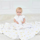 Toddler sits on a soft surface wearing a white Aden + Anais sleeping bag with a yellow and gray animal pattern.