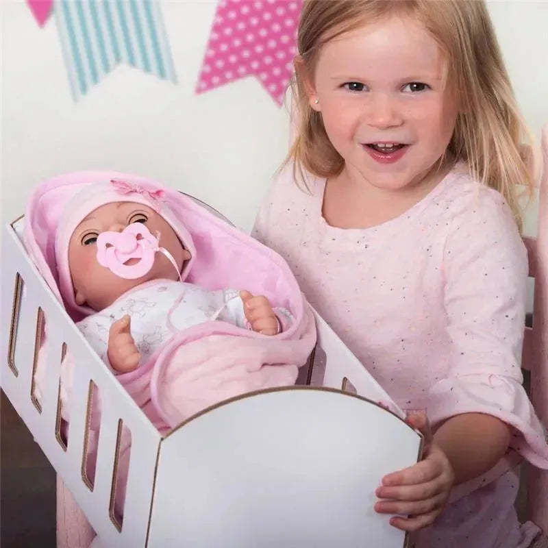 A smiling child holds a crib with the Adora Adoption Baby - Joy, a doll swaddled in pink with a pacifier.