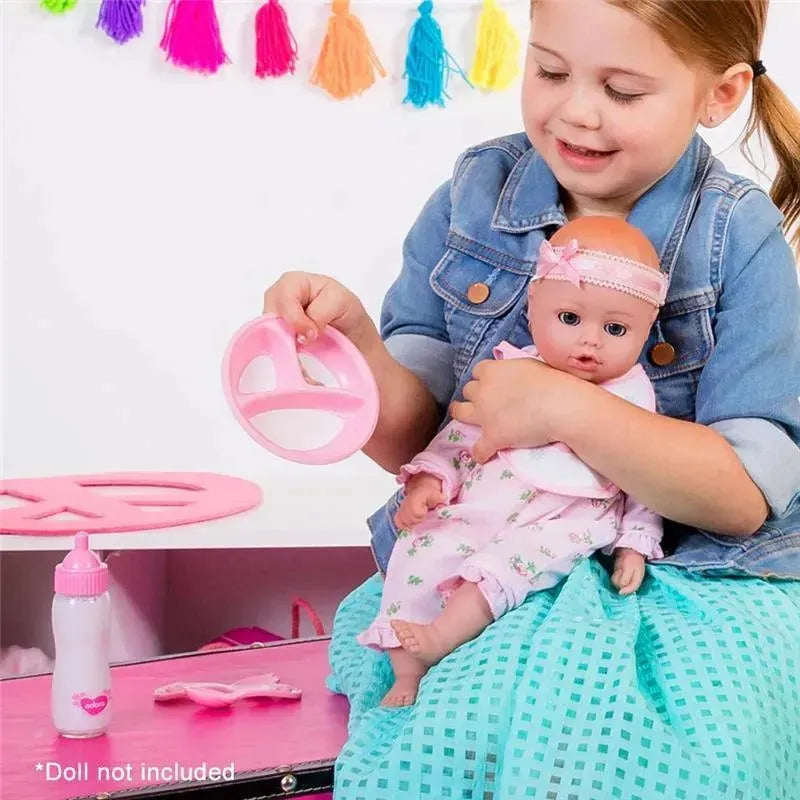 A girl in a denim jacket holds a baby doll and a pink feeding set, including a bottle, in a colorful playroom.