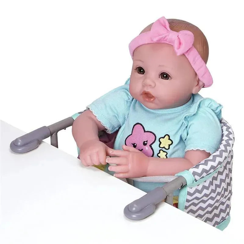 Adora Zig Zag Feeding Seat holds a doll in a high chair with a chevron pattern, featuring a light blue shirt and a pink headband.