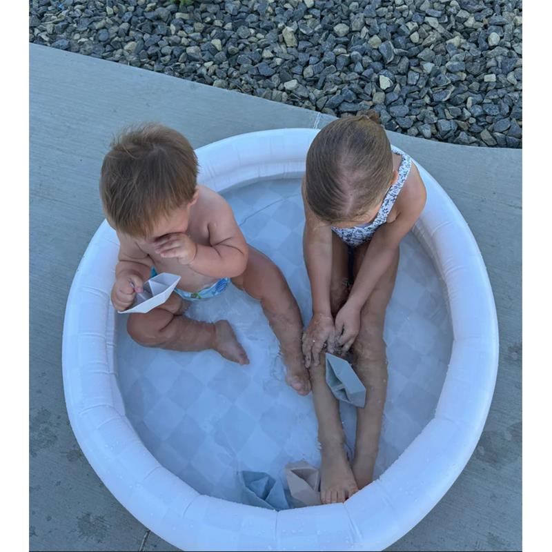 Two children play in a small inflatable pool, each holding mini paper boats, enjoying water play on a sunny day.
