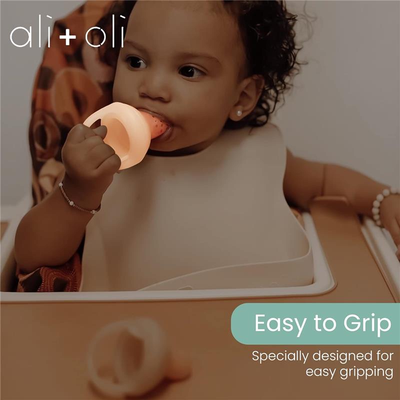 Ali + Oli Food & Fruit Feeder Pacifier, designed for easy gripping, held by a child in a high chair.