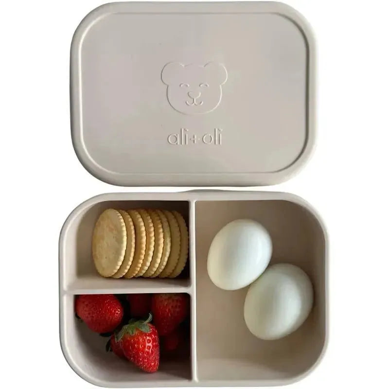 Leakproof silicone bento box featuring a bear logo, divided with strawberries, two eggs, and cookies inside.