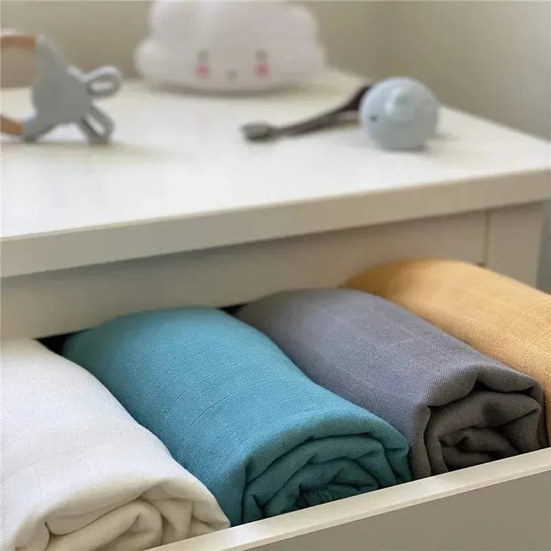 Ali + Oli muslin swaddle blankets in dream blue, gray, white, and mustard, neatly folded in a drawer.