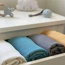 Ali + Oli muslin swaddle blankets in dream blue, gray, white, and mustard, neatly folded in a drawer.