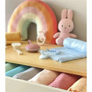 Muslin swaddle blankets in various pastel colors, with a blue blanket prominently displayed, alongside toys and accessories on a wooden surface.