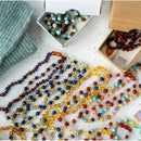 Baltic amber and rose quartz bracelets displayed among colorful beads and packaging, highlighting various styles.