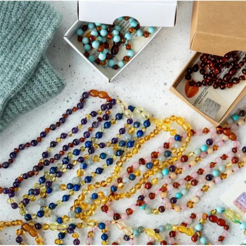 Amber Stone Baroque Baltic Amber Bracelet 173 displayed among colorful bead necklaces and packaging on a textured surface.