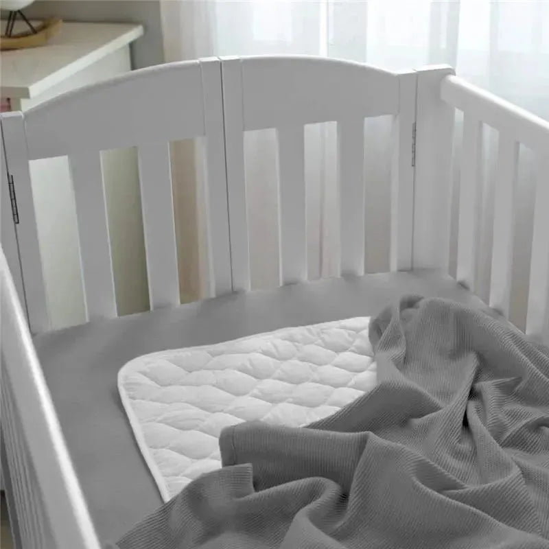 Gray waffle swaddle blanket draped over a white crib mattress with a quilted white mattress pad visible.