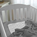Gray waffle swaddle blanket draped over a white crib mattress with a quilted white mattress pad visible.